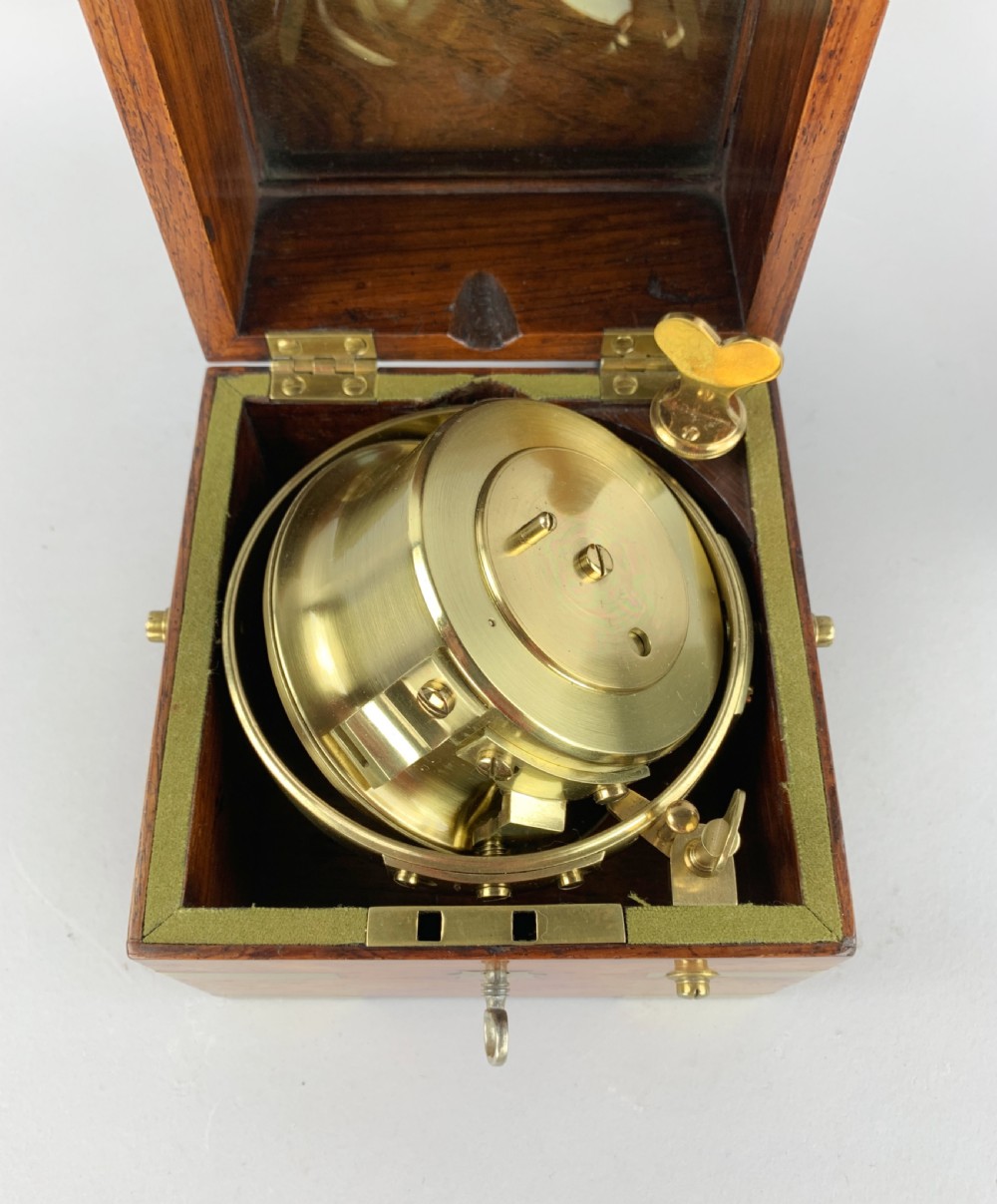 An antique 19th-century brass-bound wooden box opening to reveal a gimballed marine chronometer clock with a silvered dial and Roman numerals. View VII