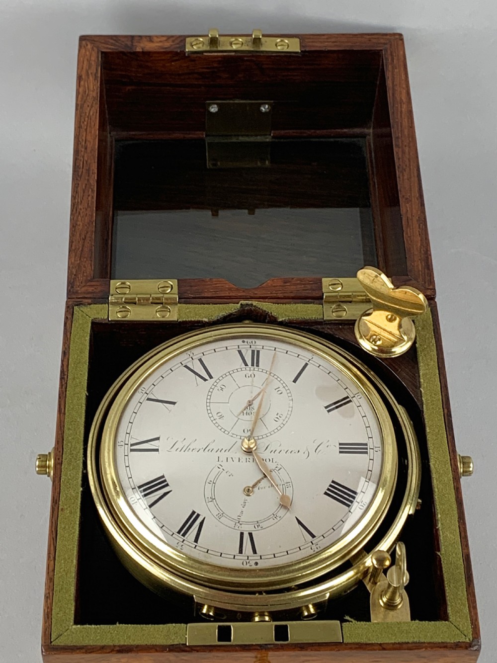 An antique 19th-century brass-bound wooden box opening to reveal a gimballed marine chronometer clock with a silvered dial and Roman numerals. View IX
