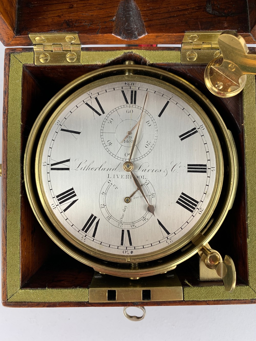 An antique 19th-century brass-bound wooden box opening to reveal a gimballed marine chronometer clock with a silvered dial and Roman numerals. View X