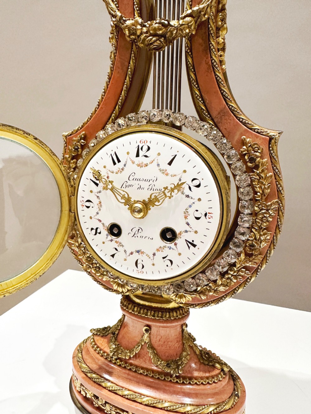 A Louis XVI style lyre-shaped mantel clock featuring pink marble, gilt bronze ormolu mounts, and a central white enamel dial. View VI