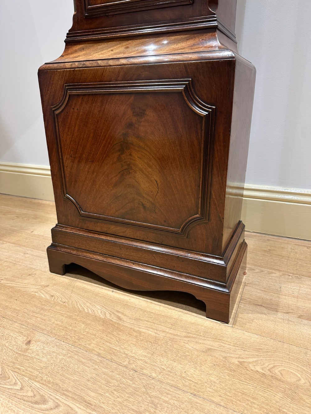 A tall Georgian flame mahogany longcase clock featuring an arched hood, brass finial, and a circular white dial with Roman numerals. View XIV