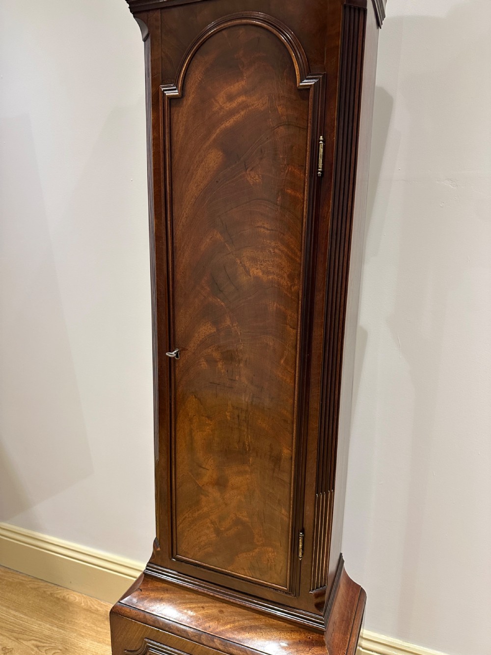 A tall Georgian flame mahogany longcase clock featuring an arched hood, brass finial, and a circular white dial with Roman numerals. View XVIII