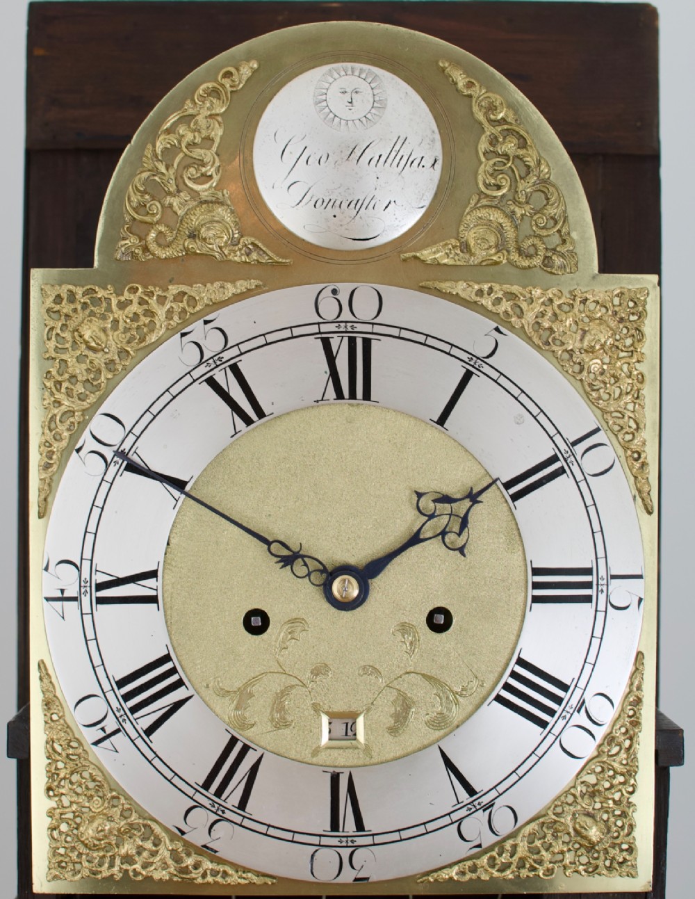 An 18th-century Georgian longcase clock featuring a dark wooden cabinet, an arched hood with a finial, and a brass dial with silvered chapter ring. View II