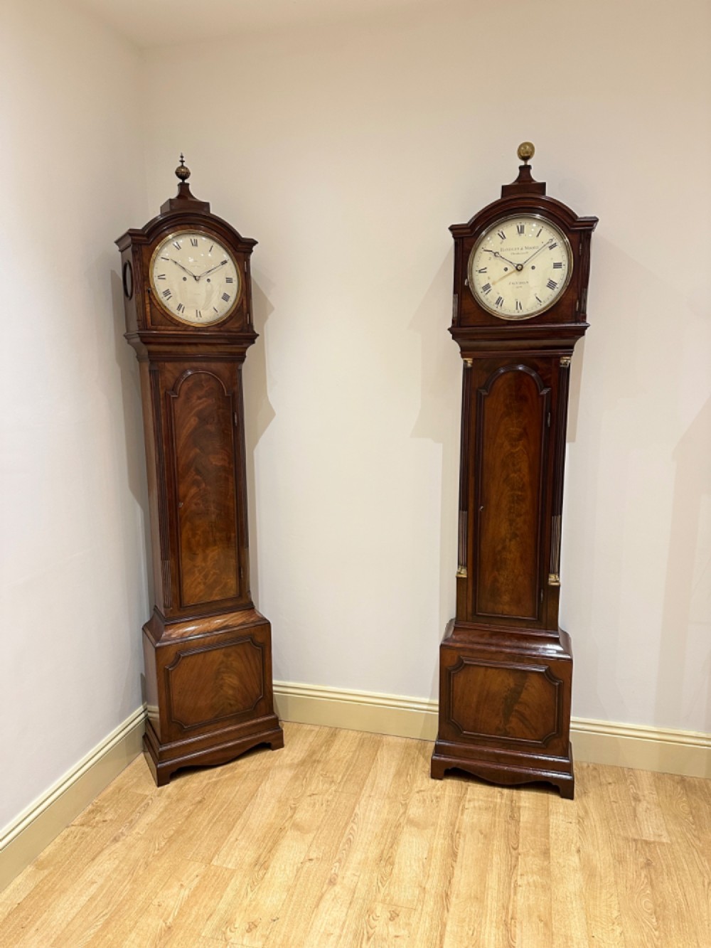 A Georgian flame mahogany longcase clock featuring an arched bonnet top with a brass ball finial, reeded columns, and an enamelled circular dial signed Handley and Moore Clerkenwell London. View V