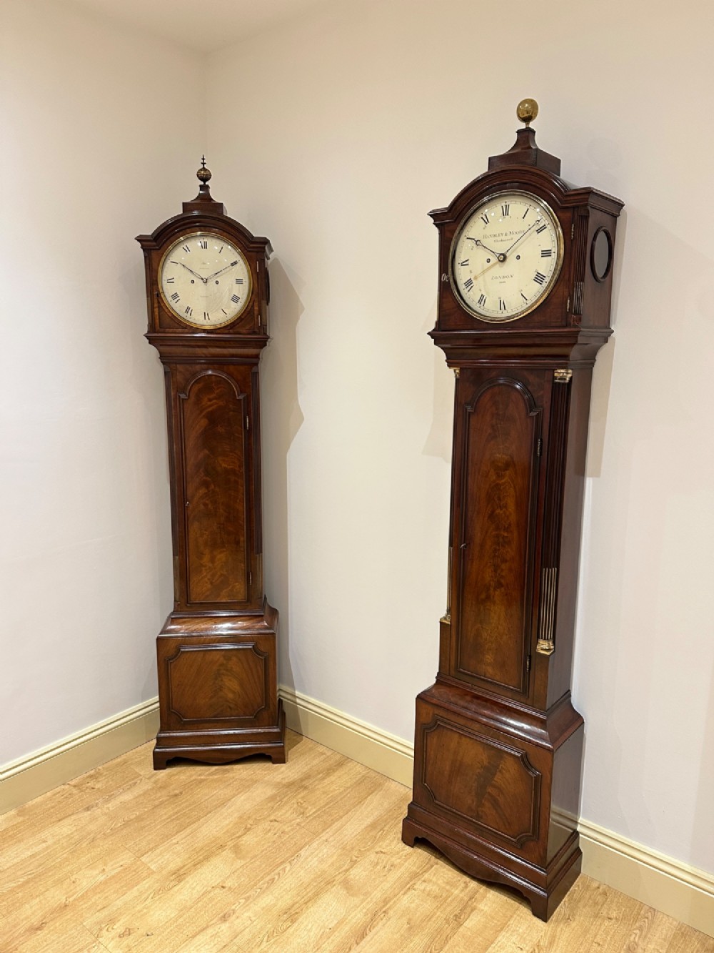 A Georgian flame mahogany longcase clock featuring an arched bonnet top with a brass ball finial, reeded columns, and an enamelled circular dial signed Handley and Moore Clerkenwell London. View VI