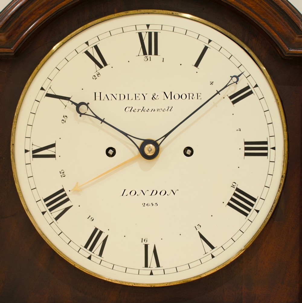 A Georgian flame mahogany longcase clock featuring an arched bonnet top with a brass ball finial, reeded columns, and an enamelled circular dial signed Handley and Moore Clerkenwell London. View VII