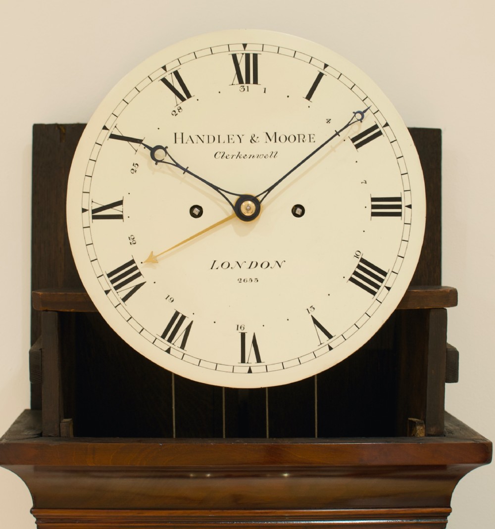 A Georgian flame mahogany longcase clock featuring an arched bonnet top with a brass ball finial, reeded columns, and an enamelled circular dial signed Handley and Moore Clerkenwell London. View VIII
