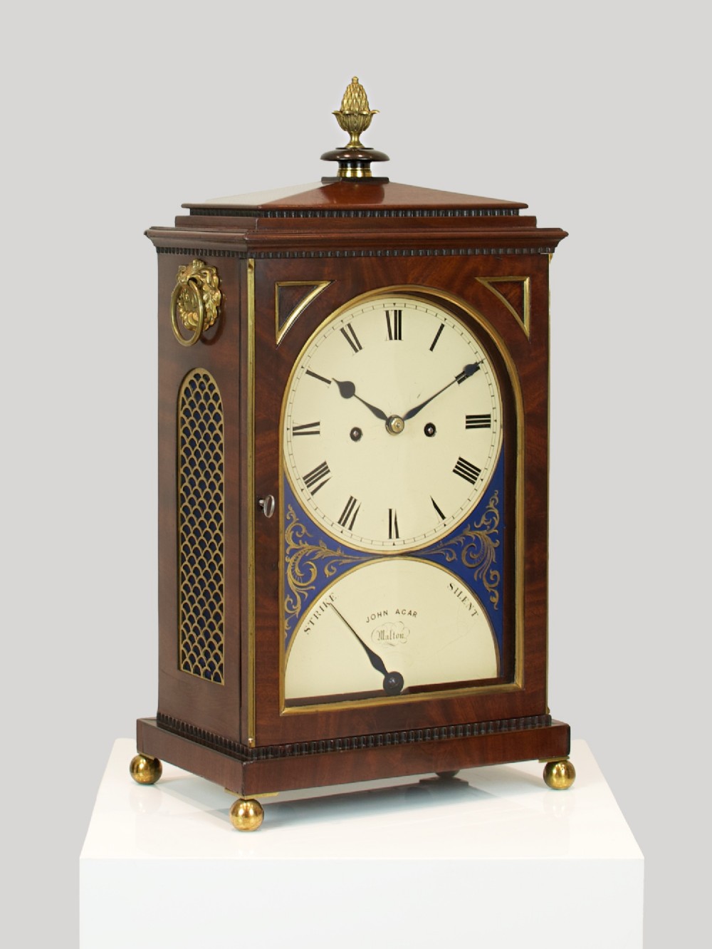 A Georgian mahogany bracket clock featuring a brass pineapple finial, brass side handles, a white dial with Roman numerals, and a lower strike-silent mechanism. View II