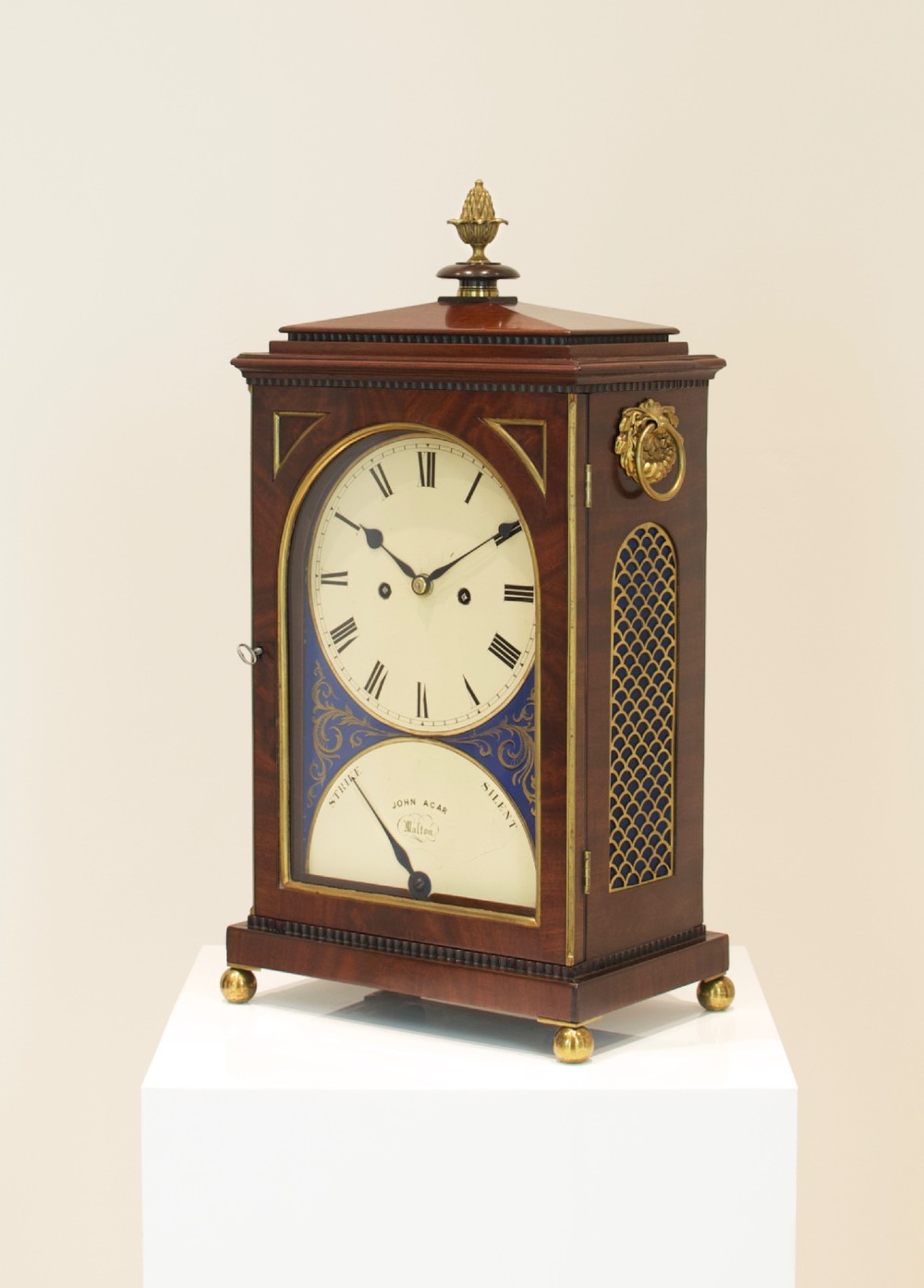 A Georgian mahogany bracket clock featuring a brass pineapple finial, brass side handles, a white dial with Roman numerals, and a lower strike-silent mechanism. View III