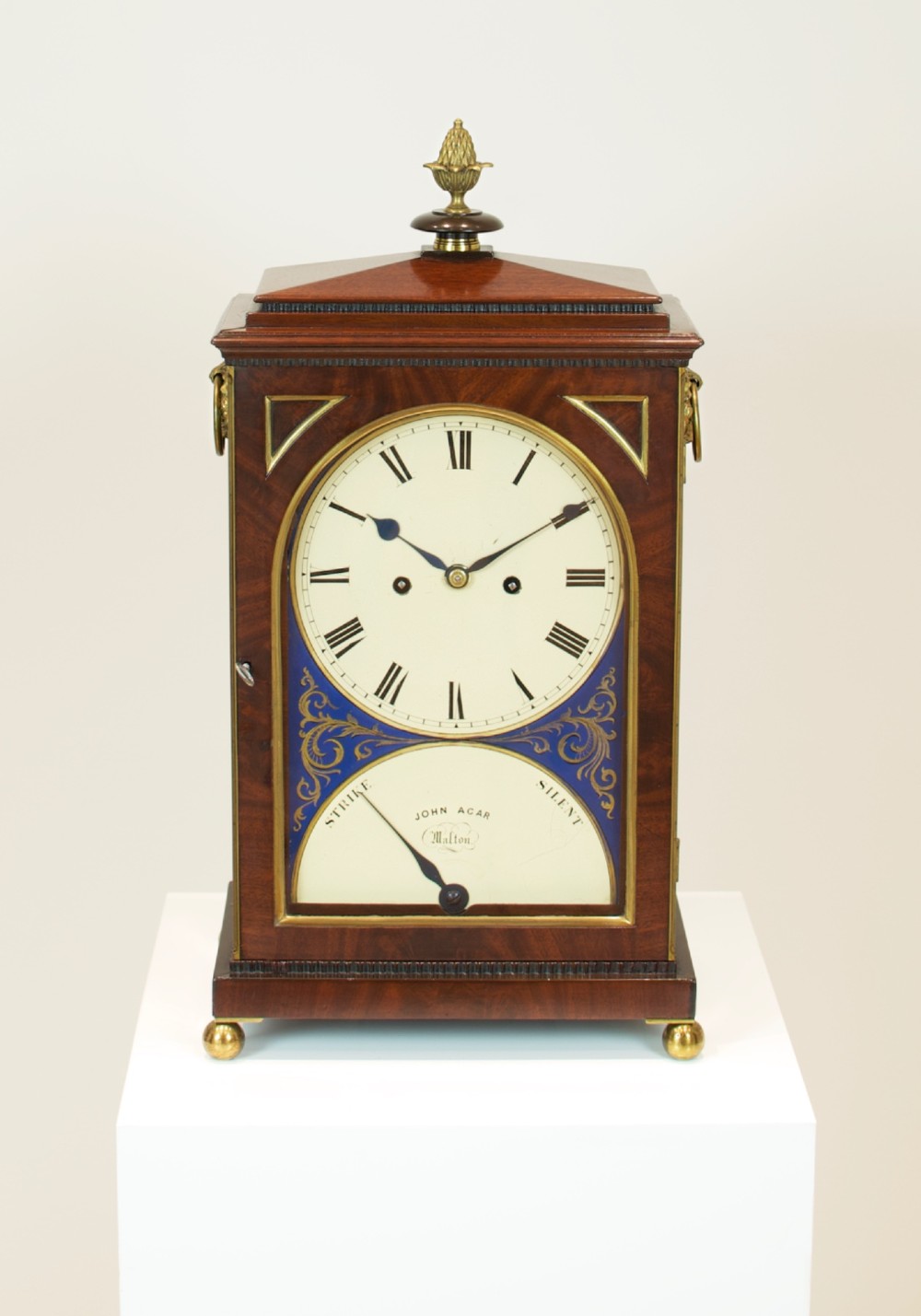 A Georgian mahogany bracket clock featuring a brass pineapple finial, brass side handles, a white dial with Roman numerals, and a lower strike-silent mechanism. View IV