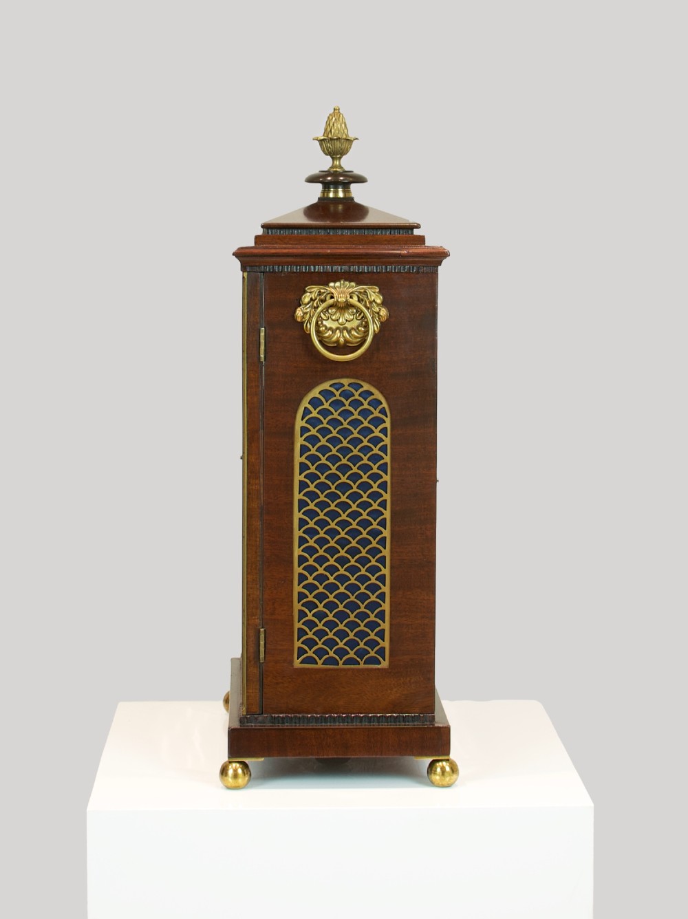 A Georgian mahogany bracket clock featuring a brass pineapple finial, brass side handles, a white dial with Roman numerals, and a lower strike-silent mechanism. View X
