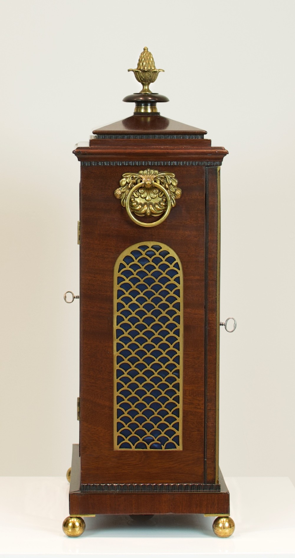 A Georgian mahogany bracket clock featuring a brass pineapple finial, brass side handles, a white dial with Roman numerals, and a lower strike-silent mechanism. View XI
