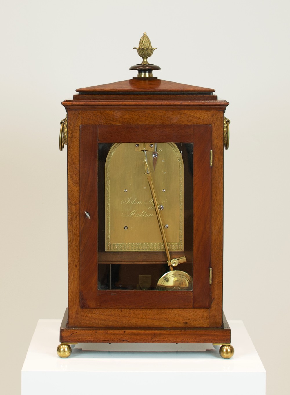 A Georgian mahogany bracket clock featuring a brass pineapple finial, brass side handles, a white dial with Roman numerals, and a lower strike-silent mechanism. View XV