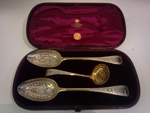 fig 1. A dark presentation case lined with purple silk containing two embossed silver-gilt berry spoons and a pierced sugar sifter spoon.