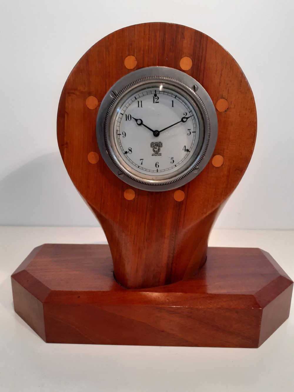 A wooden mantel clock crafted from a section of an aeroplane propeller, featuring a white clock dial marked Smiths London mounted on a chamfered timber base.