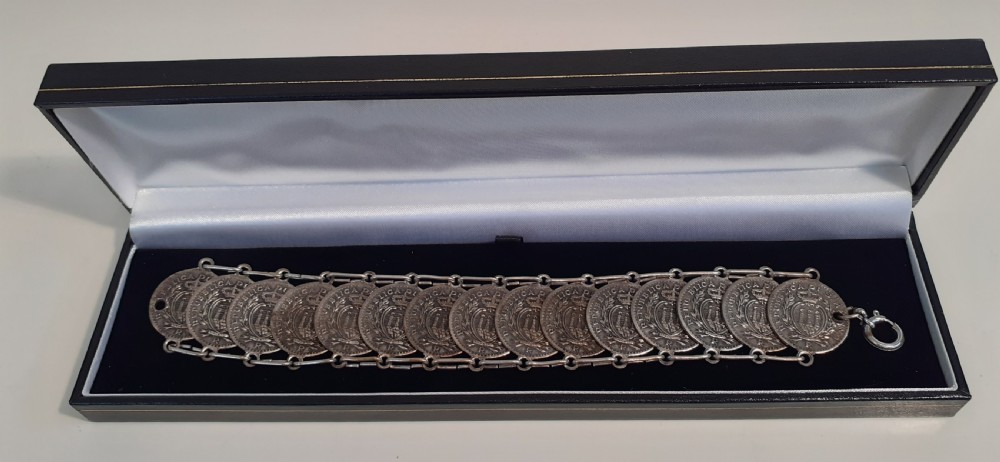 A silver bracelet crafted from fifteen overlapping San Marino ten centesimo coins joined by metal links, resting inside a presentation case.