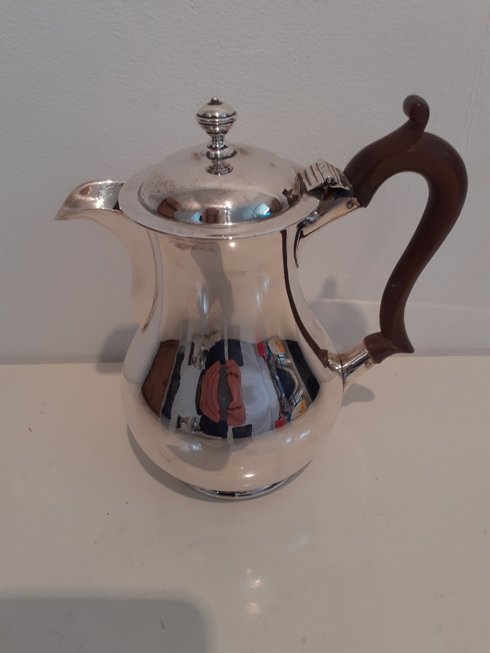 A polished silver water jug with a bulbous body, hinged lid, and a dark wooden handle against a neutral background.