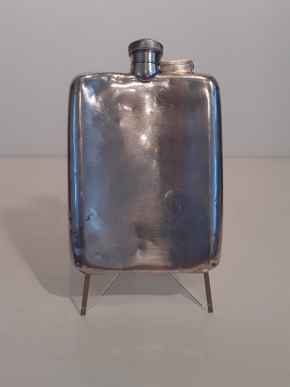 A curved silver-toned antique hip flask featuring a knurled screw cap and a patinated metal body.