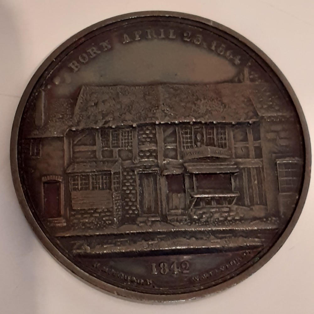 A circular dark bronze memorial medal featuring a high-relief portrait of William Shakespeare seated at a desk, flanked by inscribed text. View II