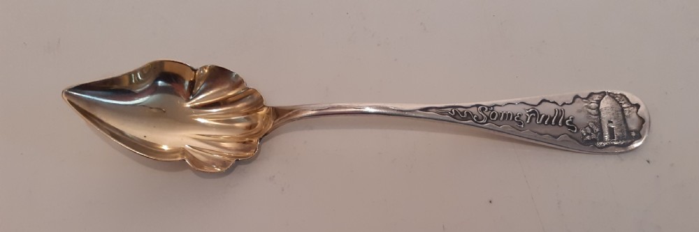 An antique sterling silver souvenir spoon featuring a gilt shell-shaped bowl and an embossed handle inscribed with Somerville and a historical building.