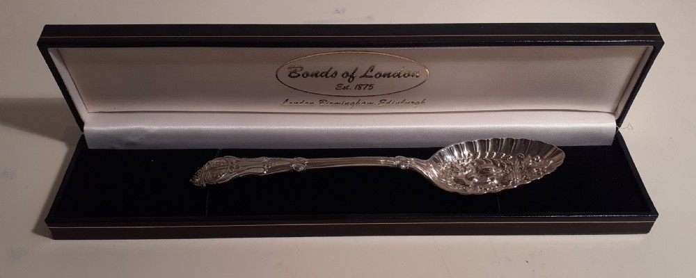 A Victorian silver plated berry spoon with an embossed fruit pattern bowl resting inside a black presentation case.