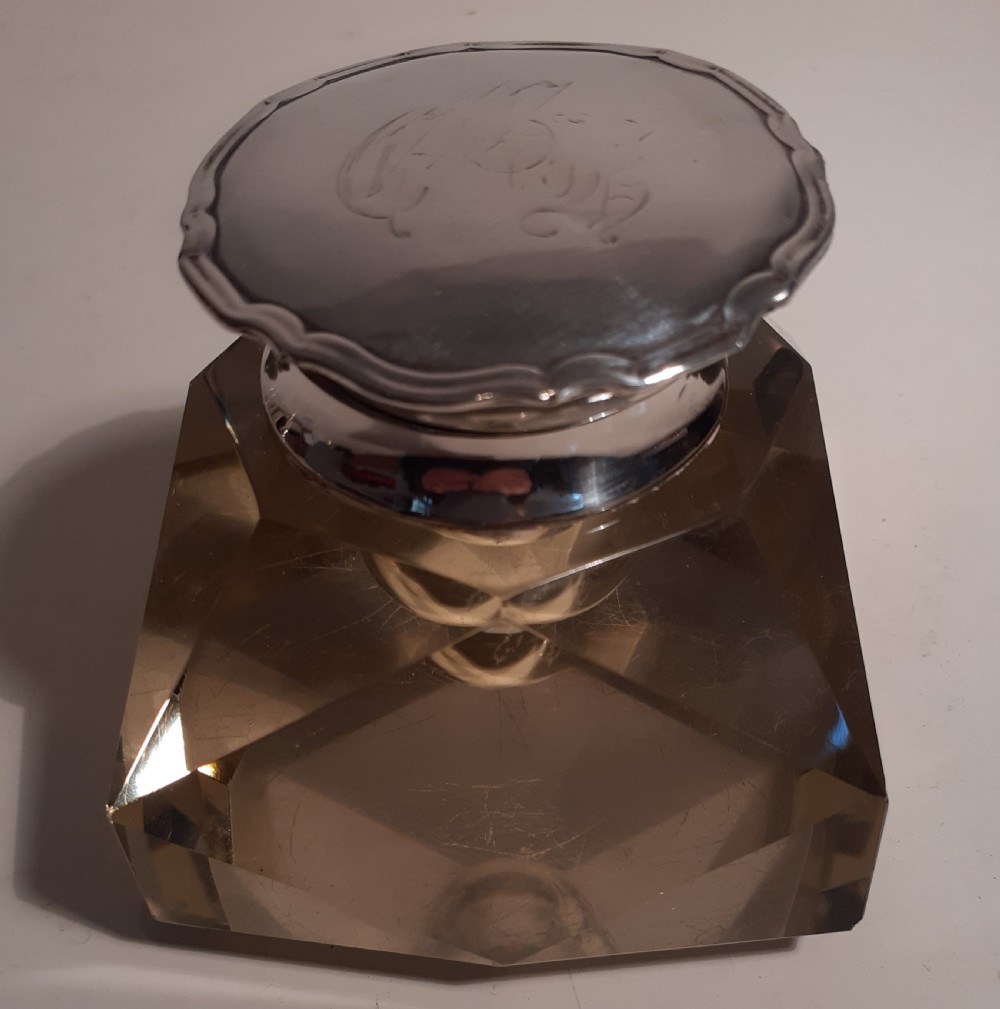 A square faceted cut crystal desktop inkwell topped with a hallmarked silver hinged lid featuring engraved monogram detailing.