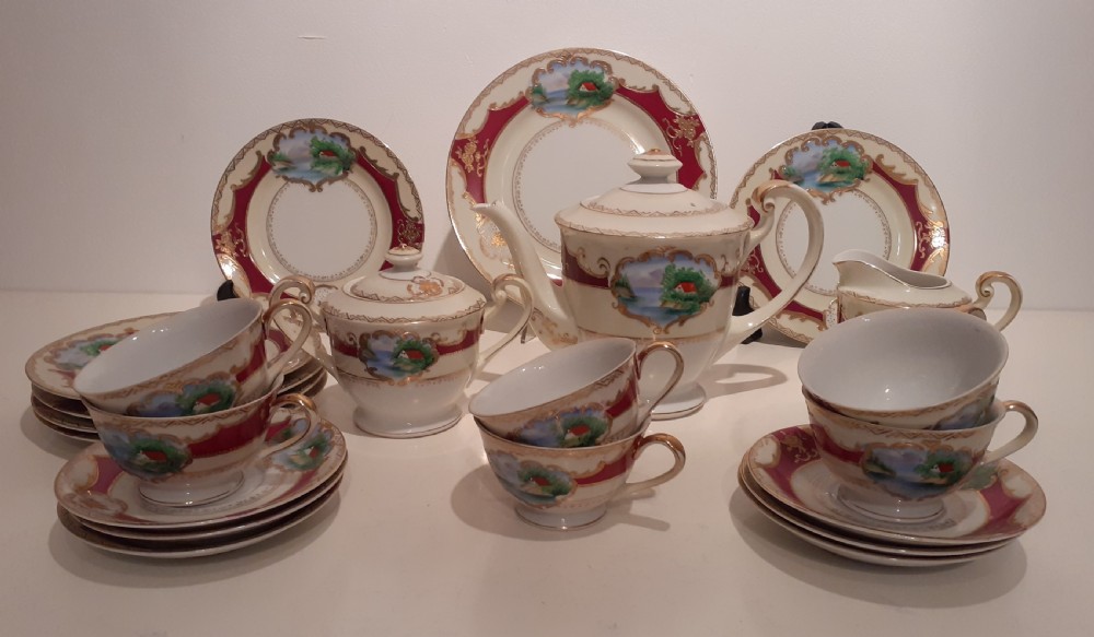 An Edwardian handpainted porcelain tea service featuring burgundy panels, gilt details, and landscape scenes including cups, saucers, plates, and a teapot.