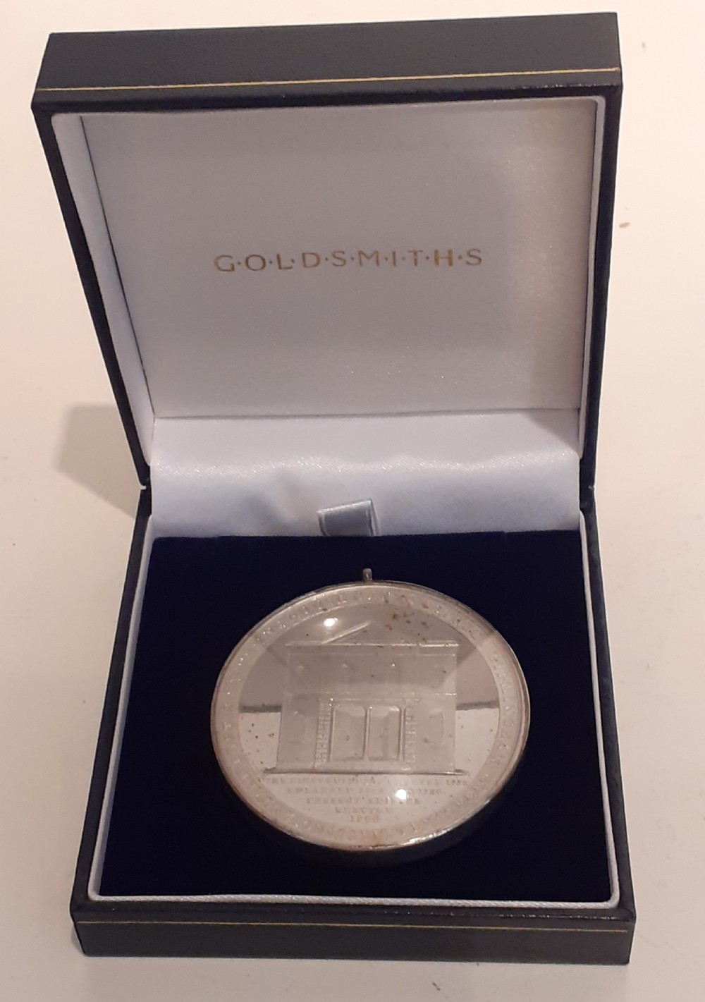 A circular Victorian silver commemorative medal featuring an engraved architectural scene, housed in a velvet-lined Goldsmiths presentation case.