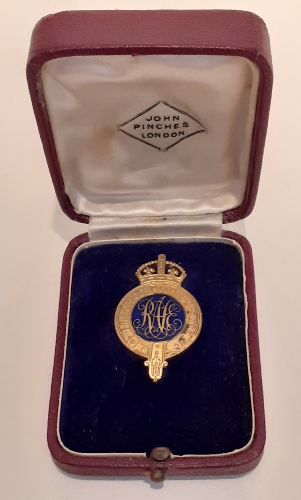 A 1930s gold-toned and blue enamel Royal Agricultural Society crowned badge displayed inside its original fitted burgundy presentation case.