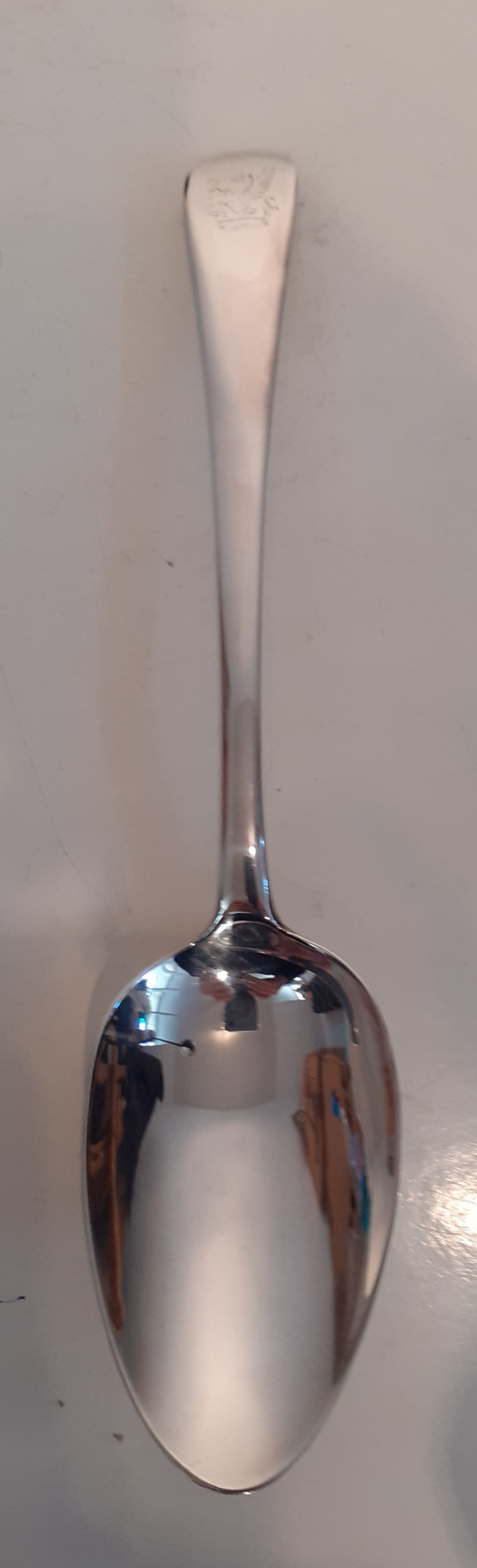 A Georgian sterling silver serving spoon featuring a polished oval bowl, narrow stem, and engraved crest at the handle terminal.