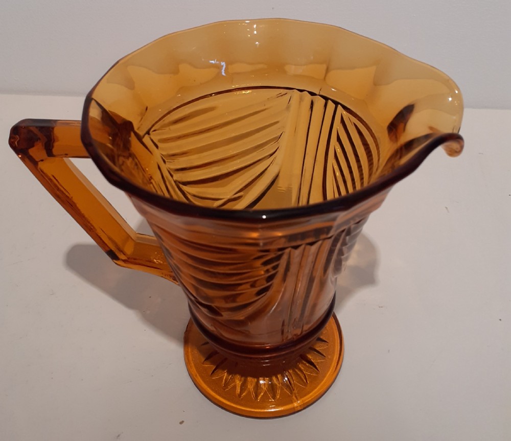 An amber-coloured Art Deco pressed glass water jug featuring geometric ribbed motifs, a flared rim, and an angular handle.