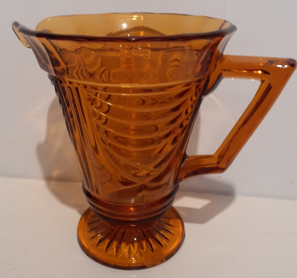 An amber-coloured Art Deco pressed glass water jug featuring geometric ribbed motifs, a flared rim, and an angular handle. View II