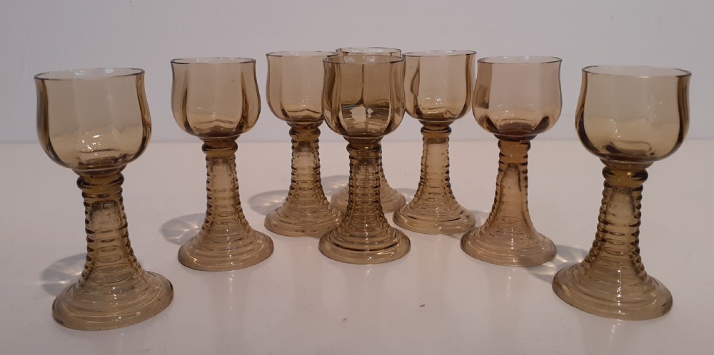 A set of seven amber tinted glass port glasses with tulip-shaped bowls and ribbed stems on circular bases.