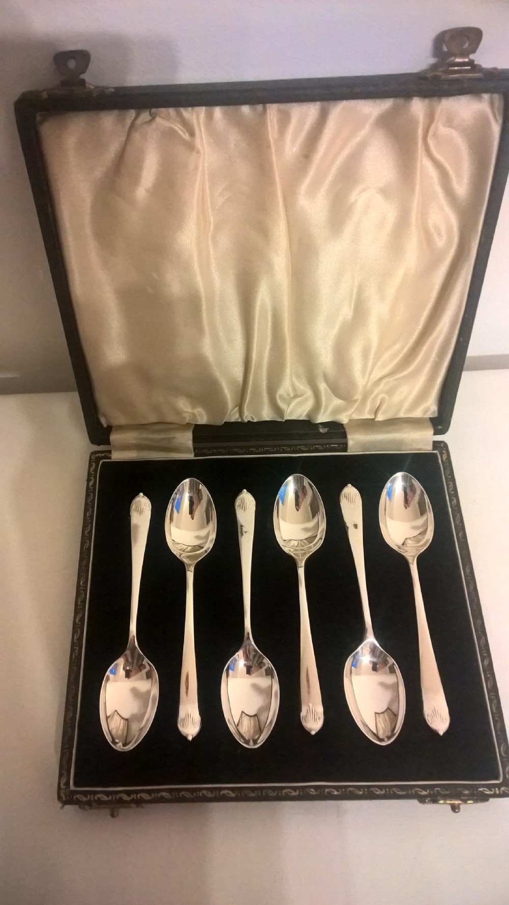 A fitted dark presentation box displaying six silver coffee spoons with flared terminals arranged on black velvet.