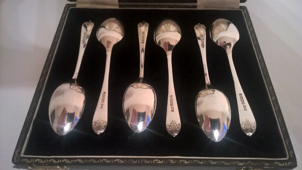 A fitted dark presentation box displaying six silver coffee spoons with flared terminals arranged on black velvet. View III