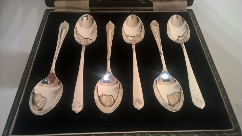 A fitted dark presentation box displaying six silver coffee spoons with flared terminals arranged on black velvet. View II