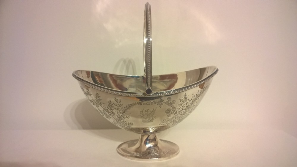 An 1877 hallmarked sterling silver pedestal sweet basket featuring an overhead handle, beaded trim, and engraved botanical motifs.