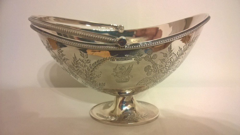 An 1877 hallmarked sterling silver pedestal sweet basket featuring an overhead handle, beaded trim, and engraved botanical motifs. View II