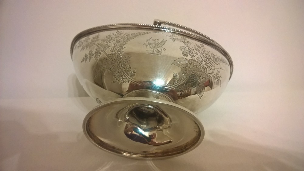 An 1877 hallmarked sterling silver pedestal sweet basket featuring an overhead handle, beaded trim, and engraved botanical motifs. View V