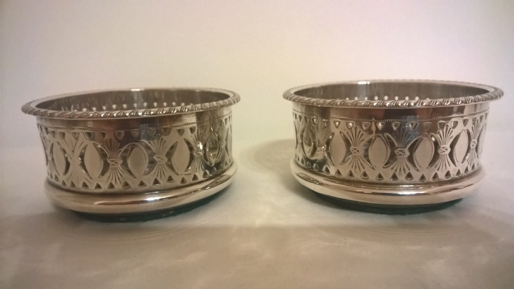 A pair of circular silver-plated wine coasters featuring pierced gallery sides, beaded borders, and turned hardwood bases.