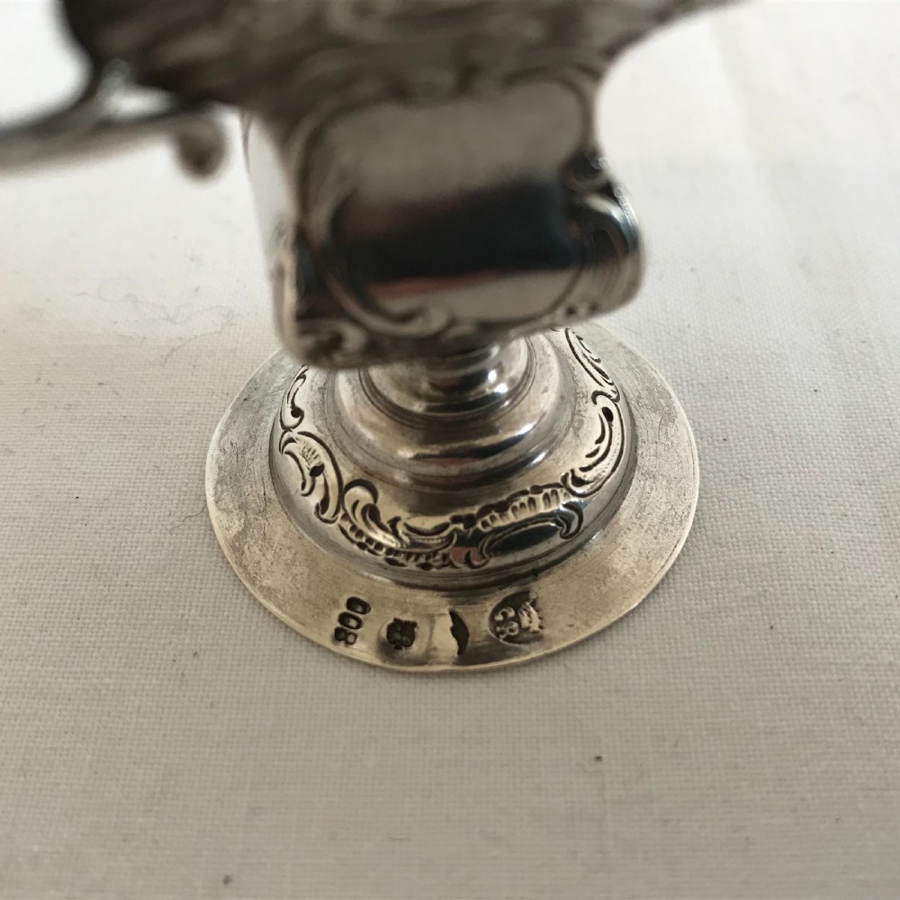An ornate German silver miniature urn vase featuring scrolled handles, floral relief chasing, and a circular pedestal base. View V