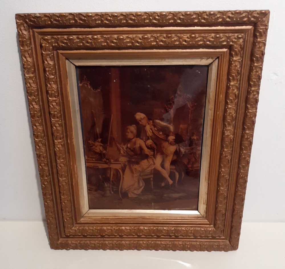 An antique framed crystoleum depicting an 18th-century style courting couple inside an ornate gold-gilded wooden frame.