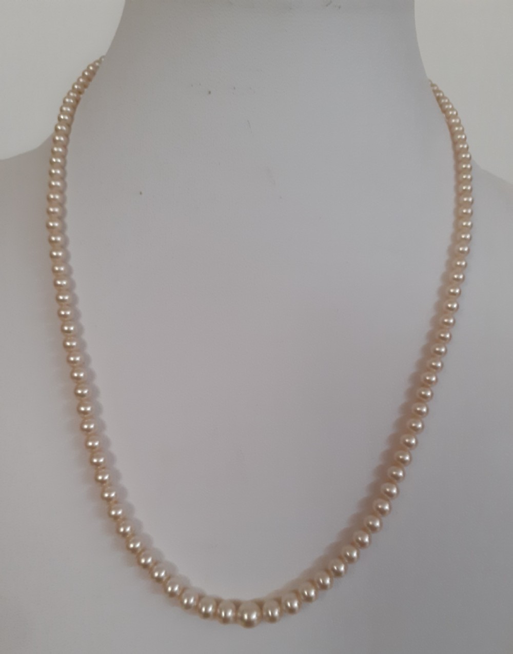 A single strand of uniform cream-coloured simulated pearls featuring a silver clasp displayed on a mannequin neck.
