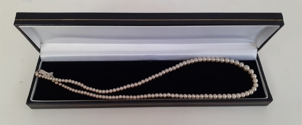 A single strand of uniform cream-coloured simulated pearls featuring a silver clasp displayed on a mannequin neck. View IV