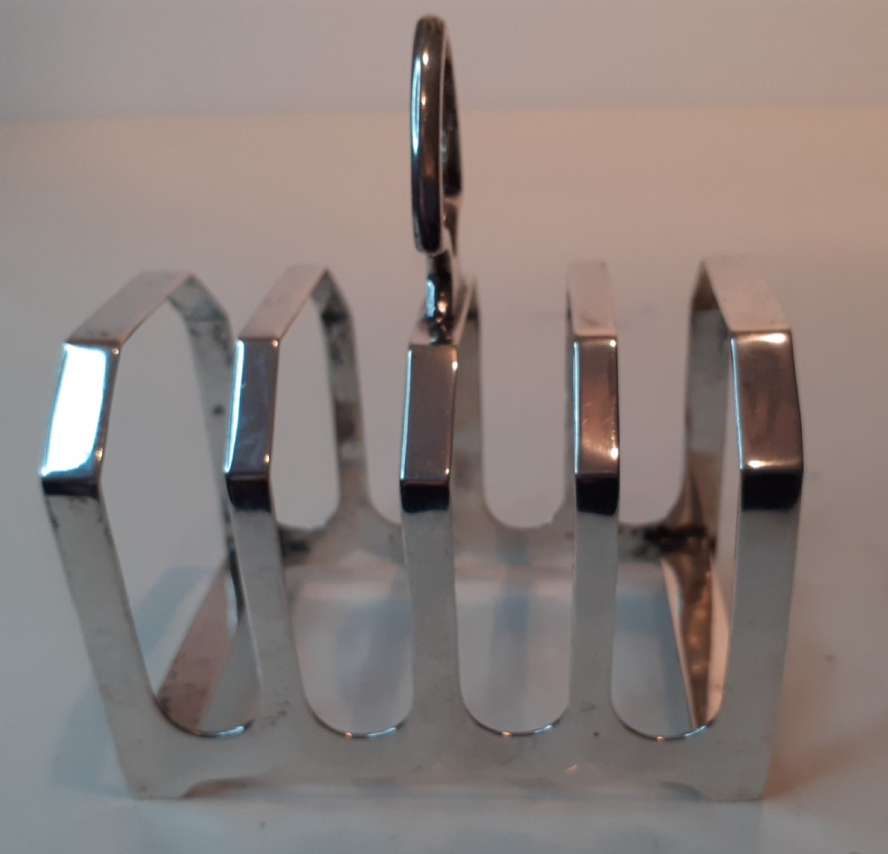 A four-slot silver toast rack featuring angular geometric arches and a central looped handle on a flat base.