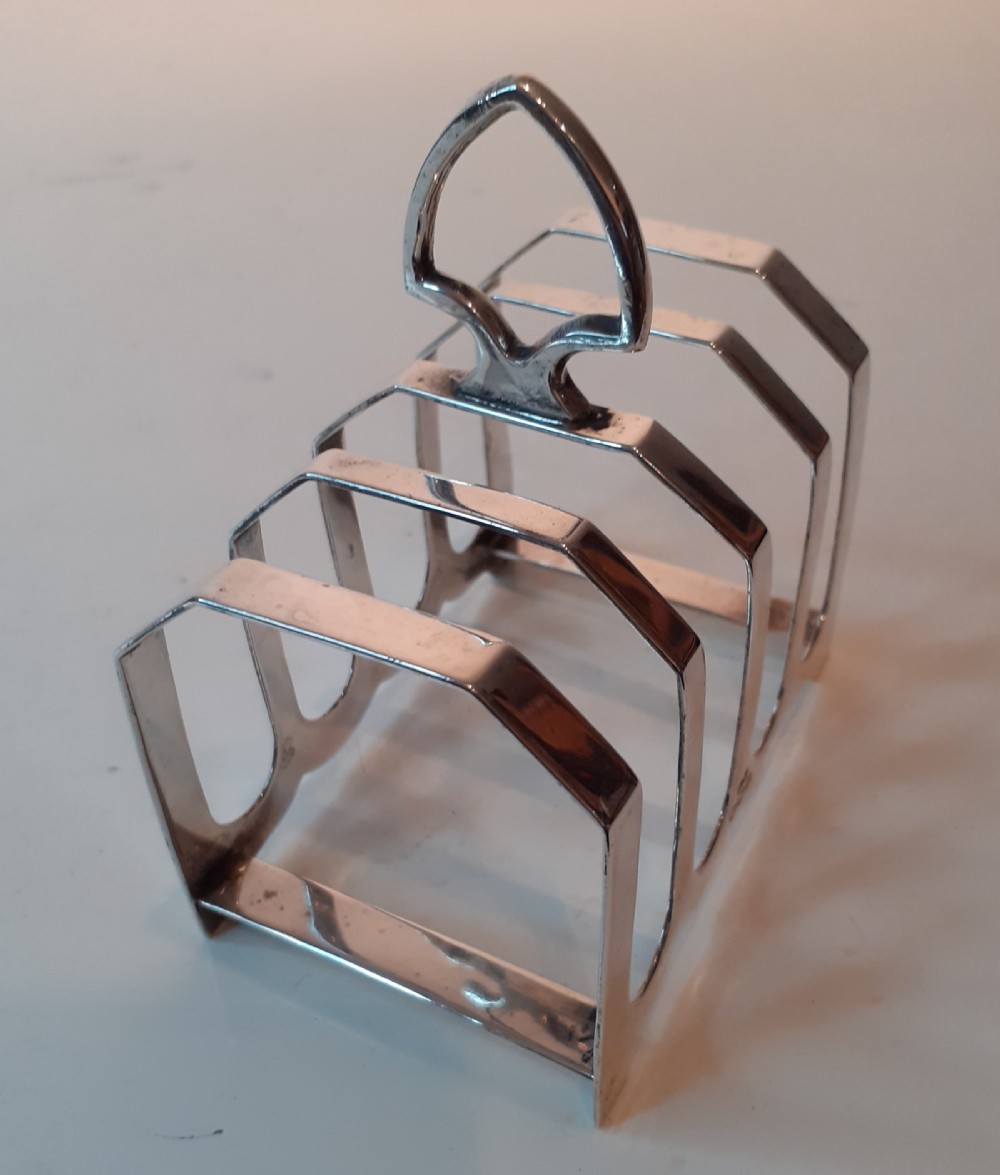 A four-slot silver toast rack featuring angular geometric arches and a central looped handle on a flat base. View II