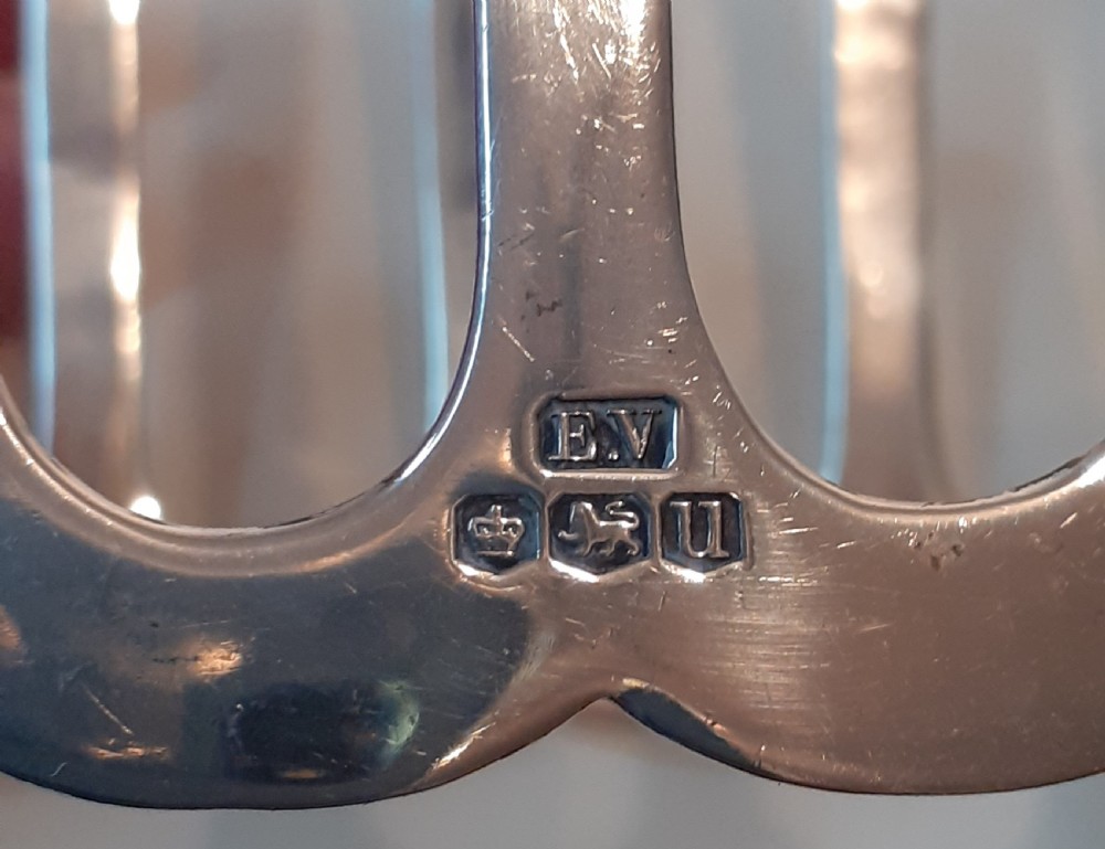 A four-slot silver toast rack featuring angular geometric arches and a central looped handle on a flat base. View III
