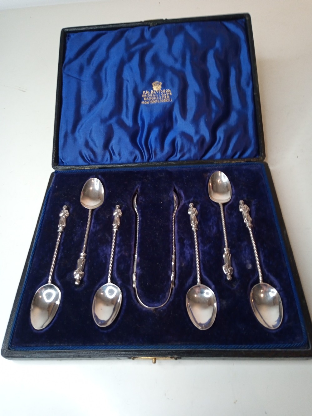 A late Victorian cased sterling silver set featuring six twisted-stem spoons with figural finials and matching sugar tongs housed in a blue velvet-lined box.