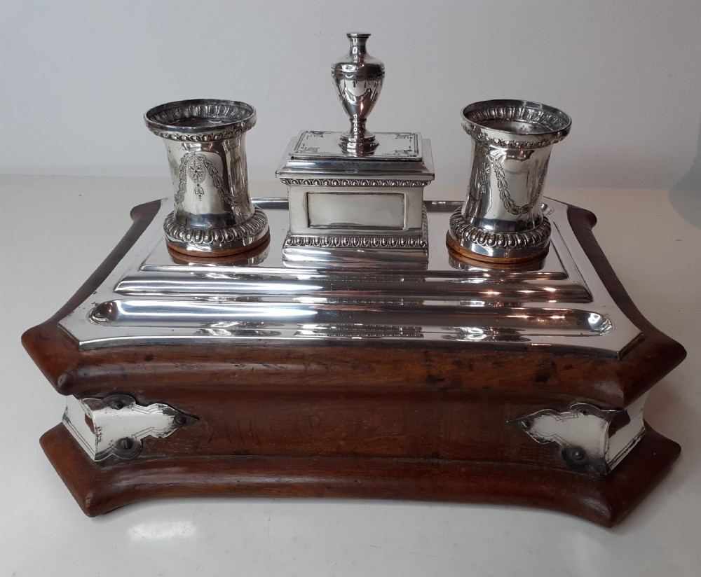 A Victorian silverplated standish featuring a shaped wooden base, two etched cylindrical inkwell holders, a central urn-topped box, and an integrated pen tray. View II
