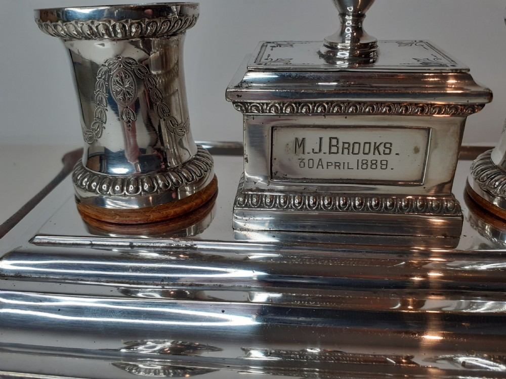 A Victorian silverplated standish featuring a shaped wooden base, two etched cylindrical inkwell holders, a central urn-topped box, and an integrated pen tray. View IV